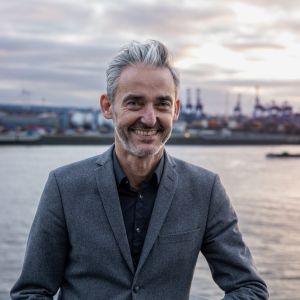 Folke Siever, Regionaldirektor bei Ginn Hotels, lächelt vor der Kulisse des Hamburger Hafens